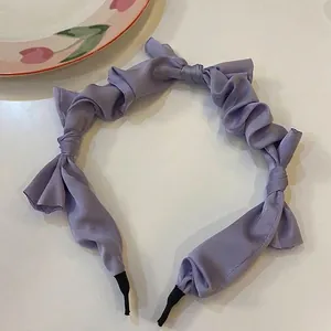 Macro shot showing the texture of a purple pleated satin headband with decorative bows