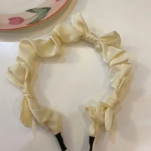 Close-up detail of a cream satin headband featuring elegant ruffles and multiple bow accents