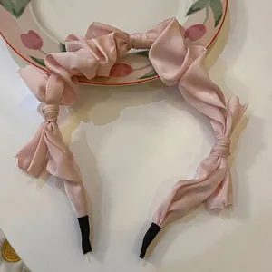 Detailed view of a pink satin bow headband with elegant ruffled design on a plate