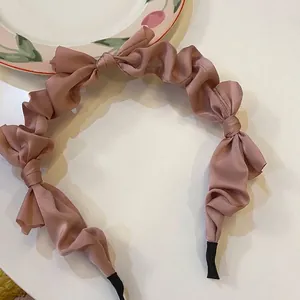 Close-up detail of a silky mauve satin pleated headband with elegant bow accents.