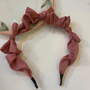 Detailed macro view of a dusky pink silk satin headband with elegant knotted bow ruffles