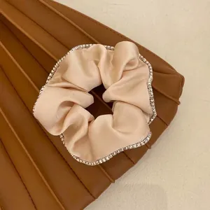 Close-up of an elegant champagne satin scrunchie with sparkling rhinestone trim
