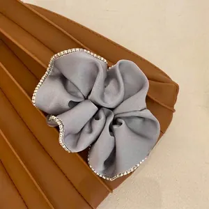Close-up detail of an elegant grey satin scrunchie featuring a sparkling rhinestone trim