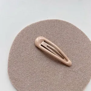 Close-up of a glossy beige snap hair clip displayed on a soft neutral textured mat
