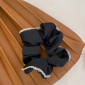 Macro detail of a black silk scrunchie with elegant sparkling rhinestone trim.