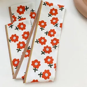 Gedetailleerd zicht op het oranje bloemmotief op een witte zijden haarsjaal lint.