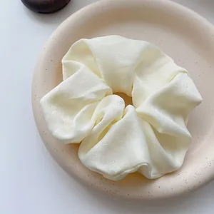 Macro view of a soft cream-colored satin large hair scrunchie on a decorative plate