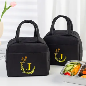 Black insulated lunch bags with golden letter J print beside a fresh meal box.