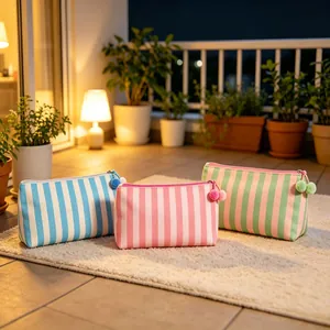 Set van drie gestreepte cosmetica tassen met pompon ritsen op een beige tapijt.