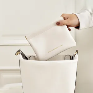 Detail of cream leather shrapnel pouch being placed in a white bucket bag