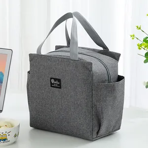 Detail view of grey insulated lunch bag with handles and side pockets on a desk