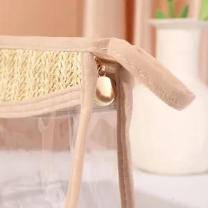 Detail view of golden zipper pull and woven straw trim on transparent PVC makeup bag.