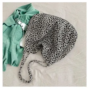 Slouchy leopard print canvas tote bag laid on fabric background with green clothing