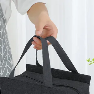 Hand holding the reinforced webbed handle of a portable black insulated lunch bag.
