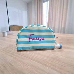 Detail van gestreepte canvas make-uptas in schelpvorm met paars Farisa-borduurwerk erop