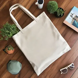 Bolsa de lona color crema lisa sobre suelo de madera con accesorios de estilo de vida.
