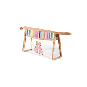 Detail of a transparent PVC makeup bag featuring rainbow straw trim and a pink letter A.