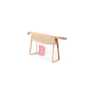 Detail of transparent PVC makeup bag with pink letter B embroidery and straw trim.