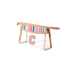 Clear PVC makeup bag with pink letter C patch and rainbow woven straw trim detail.