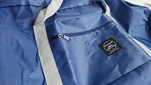 Close-up detail showing the durable zipper and woven brand label on a blue nylon travel bag