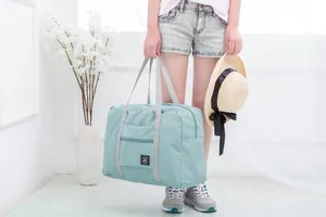 Detail view of a large foldable teal travel bag held by a model with a straw hat.