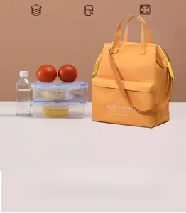 Insulated yellow lunch bag with shoulder strap shown with lunch boxes and water.