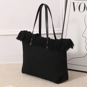 Vista detallada de un bolso tote de lona negro con elegantes acentos de flecos densos