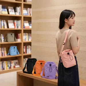 Multiple colors of nylon drawstring crossbody bags shown in a lifestyle library setting