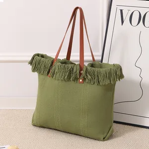 Primer plano de un bolso tote de lona verde tejida con flecos y asas de color marrón.