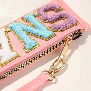 Close-up detail of a pink fabric pouch with colorful chenille letter embroidery patches.