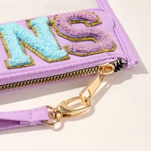 Close-up detail of purple storage bag with chenille embroidery letters and gold zipper