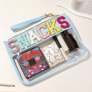 Close-up view of a clear light blue PVC makeup bag with chenille SNACKS letters