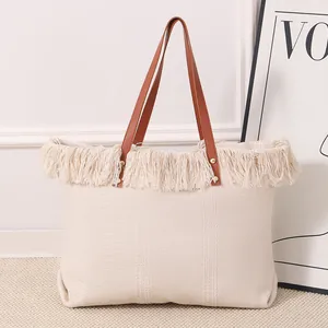 Detalle de un bolso tote grande de lona con flecos bohemios y asas de cuero