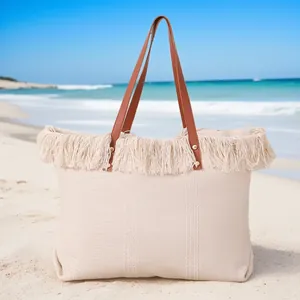 Bolso de playa grande tejido en color crema con flecos sobre arena soleada