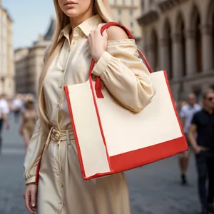 Close-up of a stylish cream canvas tote bag with red trim carried by a model