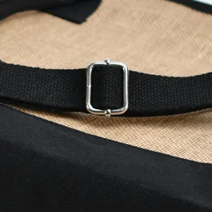 Primo piano della fibbia regolabile in metallo sulla tracolla nera di una borsa in juta.
