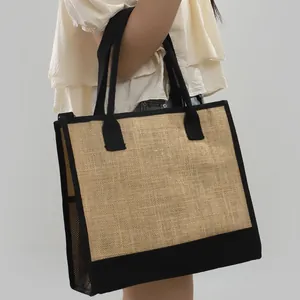 Grande borsa tote in iuta con rifiniture nere mostrata sulla spalla di una modella.
