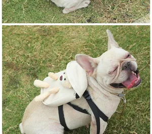 Close-up of a French Bulldog wearing a beige pet backpack with a plush bear on grass.