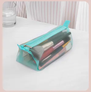 Detail view of a mint green mesh cosmetic pouch filled with makeup brushes on a white table.