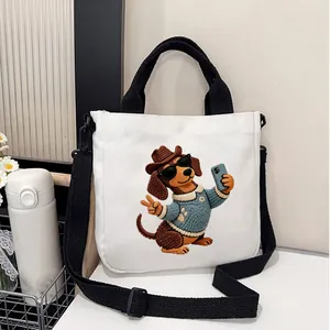 Close-up detail of cute dachshund dog cartoon embroidery on white canvas crossbody tote bag