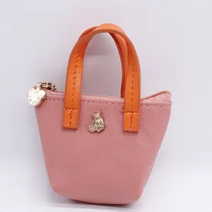 Mini porte-monnaie rose en cuir avec anses orange et breloque en forme d'ours doré.
