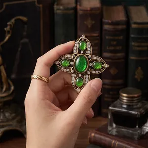 Vintage hollow cross brooch with green emerald gemstones and sparkling crystal accents.