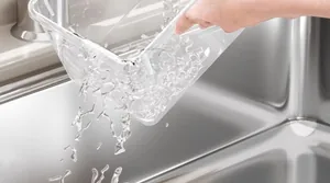 Clear plastic food storage box being rinsed with clean water in a stainless steel sink