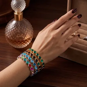 Set of colorful heart-shaped alloy bracelets worn on a wrist beside a perfume bottle