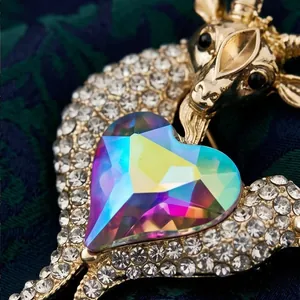 Detailed gold goat brooch featuring an iridescent heart gemstone and sparkling rhinestones.