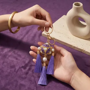 Detail of a purple embroidered ball keychain with long silk tassels and pearls.