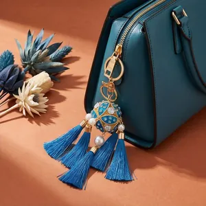 Close-up detail of a blue hydrangea tassel charm with pearls on a teal luxury handbag
