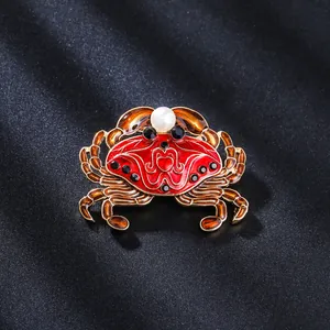 Detailansicht einer roten Emaille-Krabbenbrosche mit Perle und goldfarbenem Metallfinish