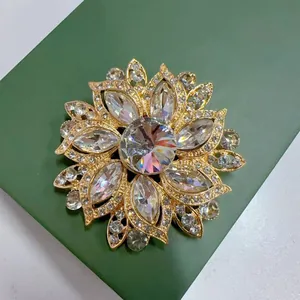 Nahaufnahme einer Vintage-Kristallblumenbrosche mit Goldfassung auf einer grünen Geschenkbox.