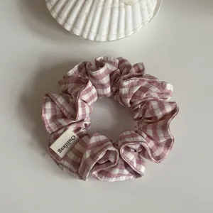 Vista detallada de un coletero tipo scrunchie de cuadros rosa y blanco con etiqueta